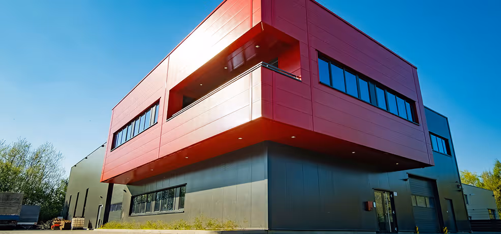 Modern two-story commercial building with a red upper section and gray lower section under a clear blue sky.