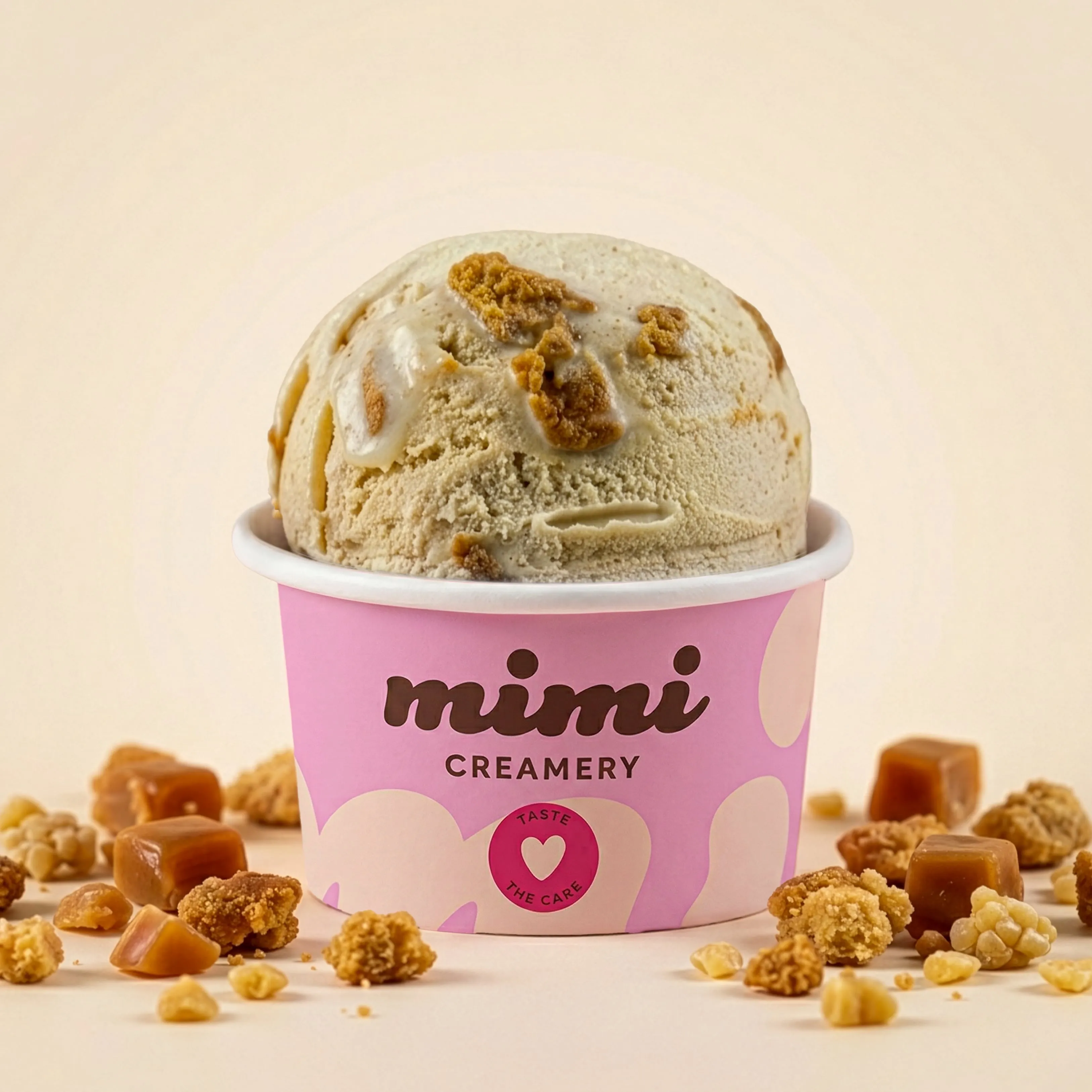 Scooped ice cream with caramel and crumb toppings in a pink Mimi Creamery cup on a light background.