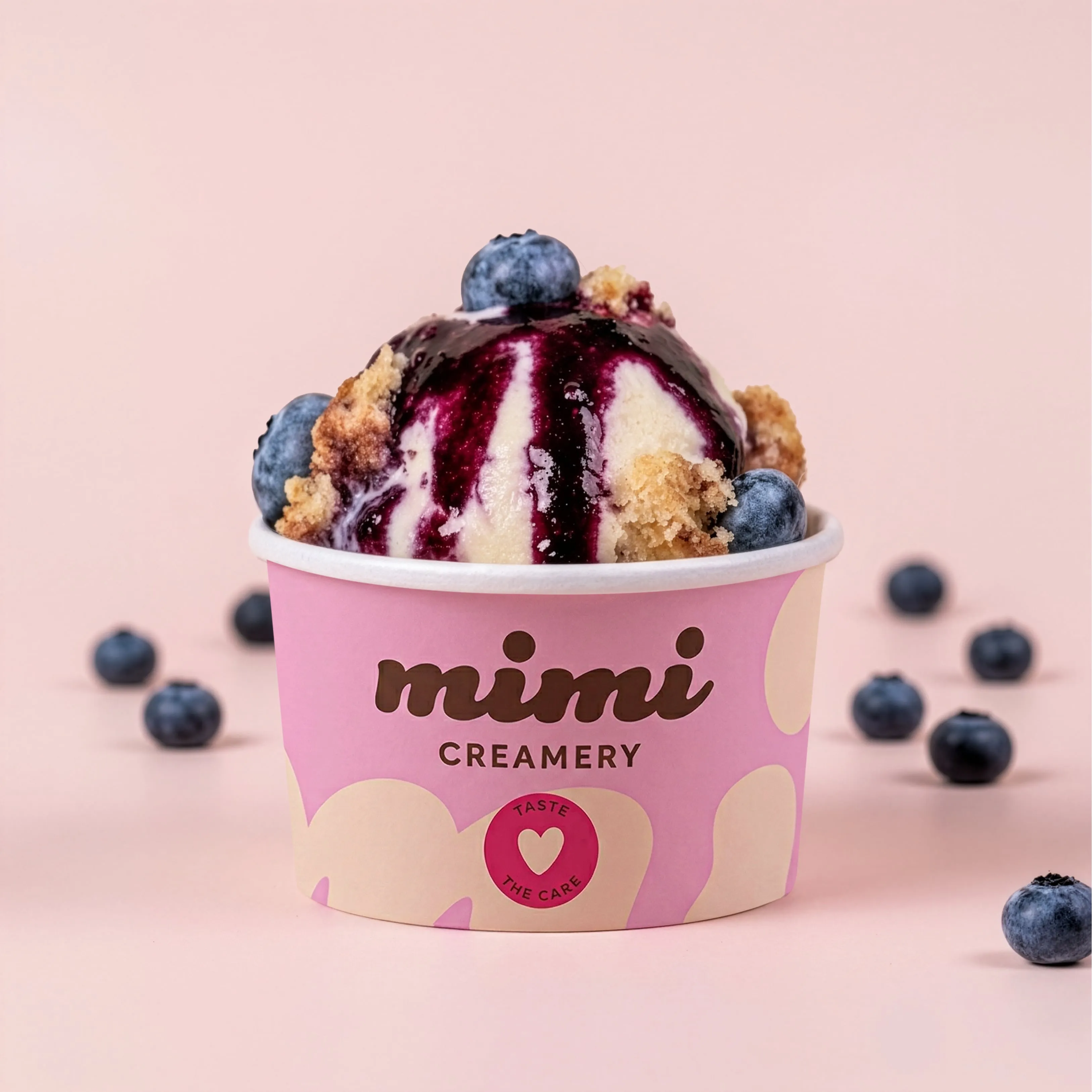 Cup of creamy blueberry cobbler ice cream with crumble and fresh blueberries on pink background.