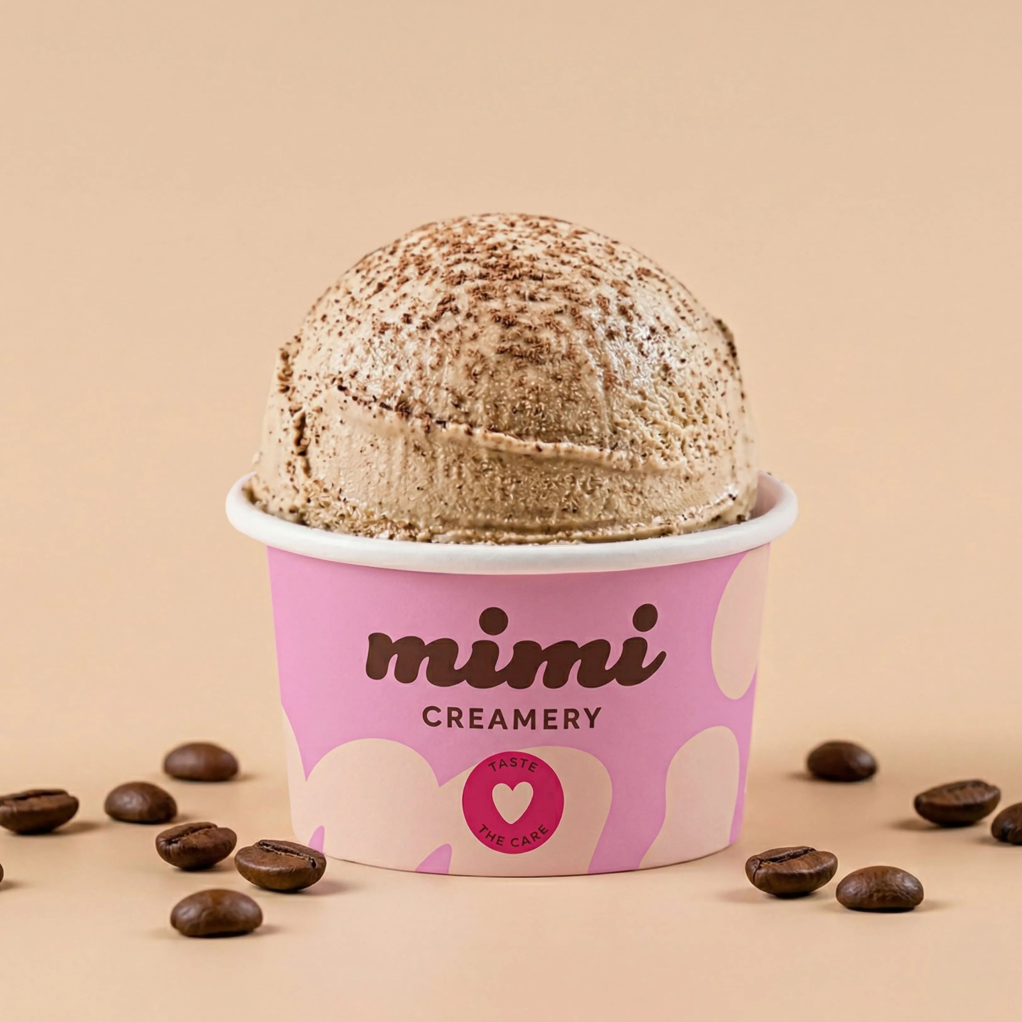 Single scoop of coffee ice cream in a pink Mimi Creamery cup surrounded by coffee beans.