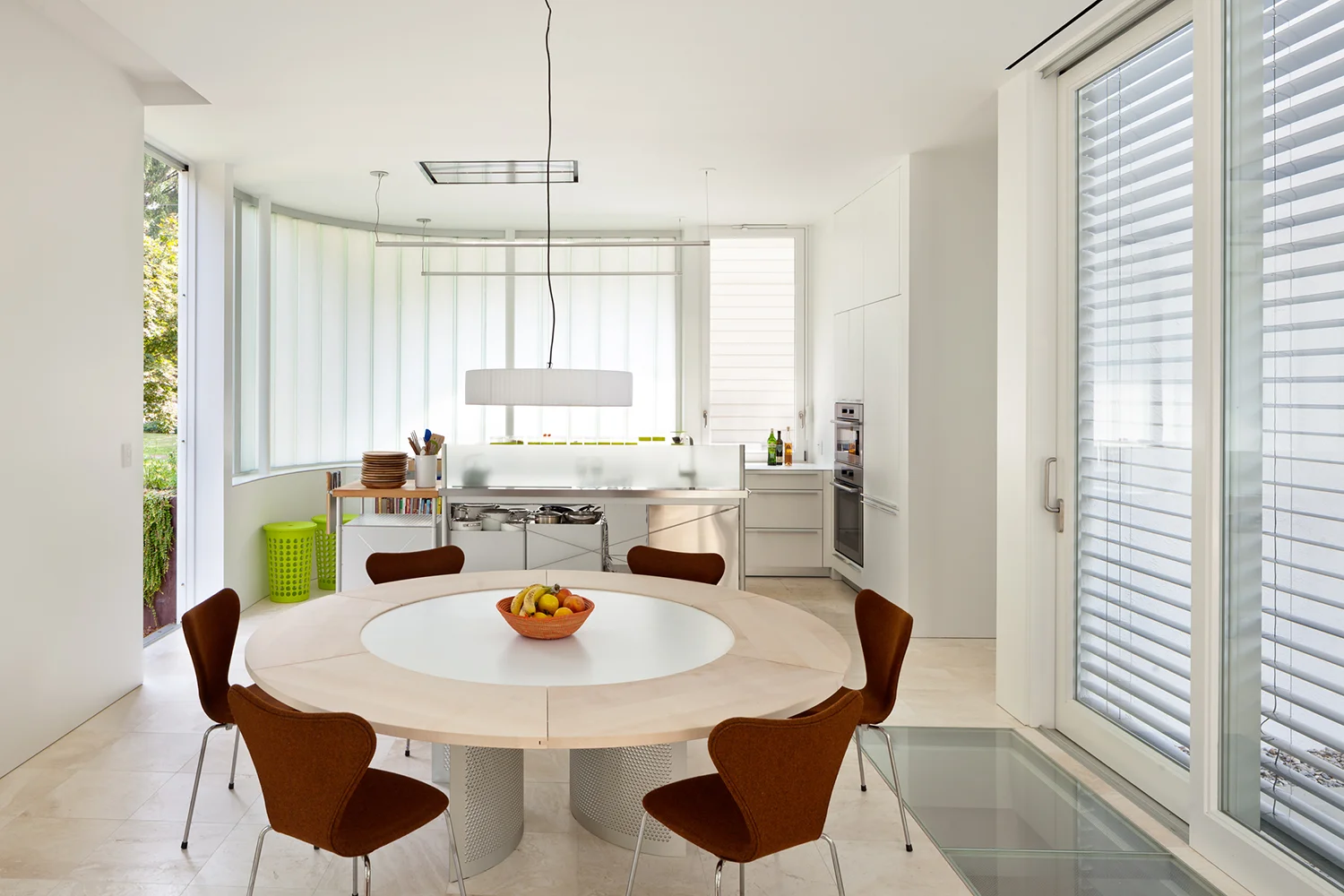A modern dining room and kitchen light filled with a wall of curved channel glass. 