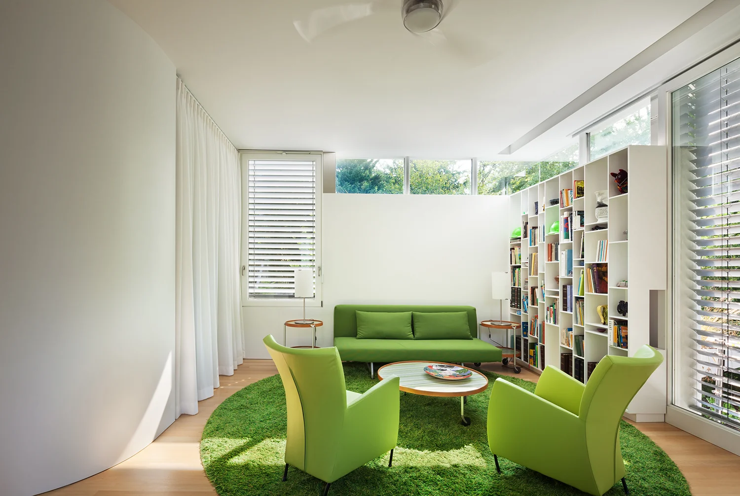 A library with green furniture and rug and clerestory windows letting in light.
