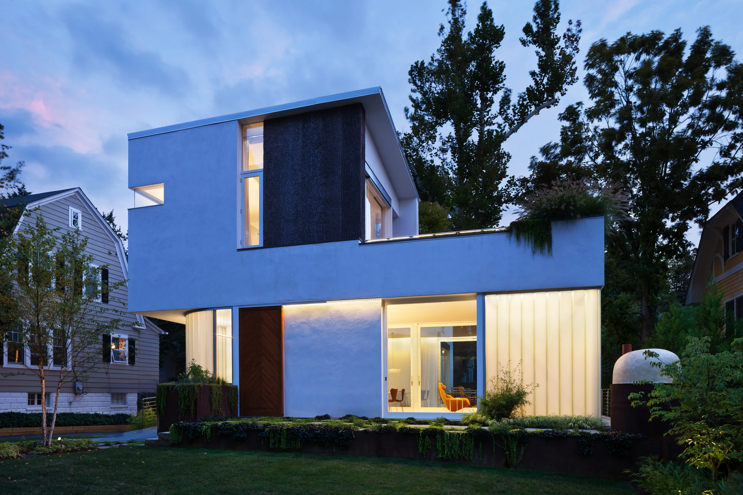 A modern white stucco house aglow with lighting during the blue hour.