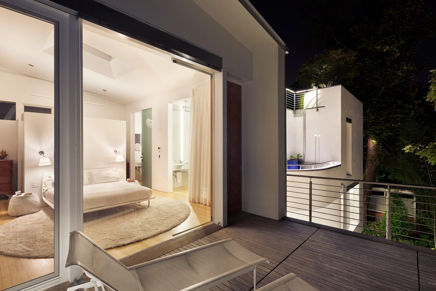 A view from the 2nd story deck to the primary bedroom, white wall and furniture with light oak flooring.