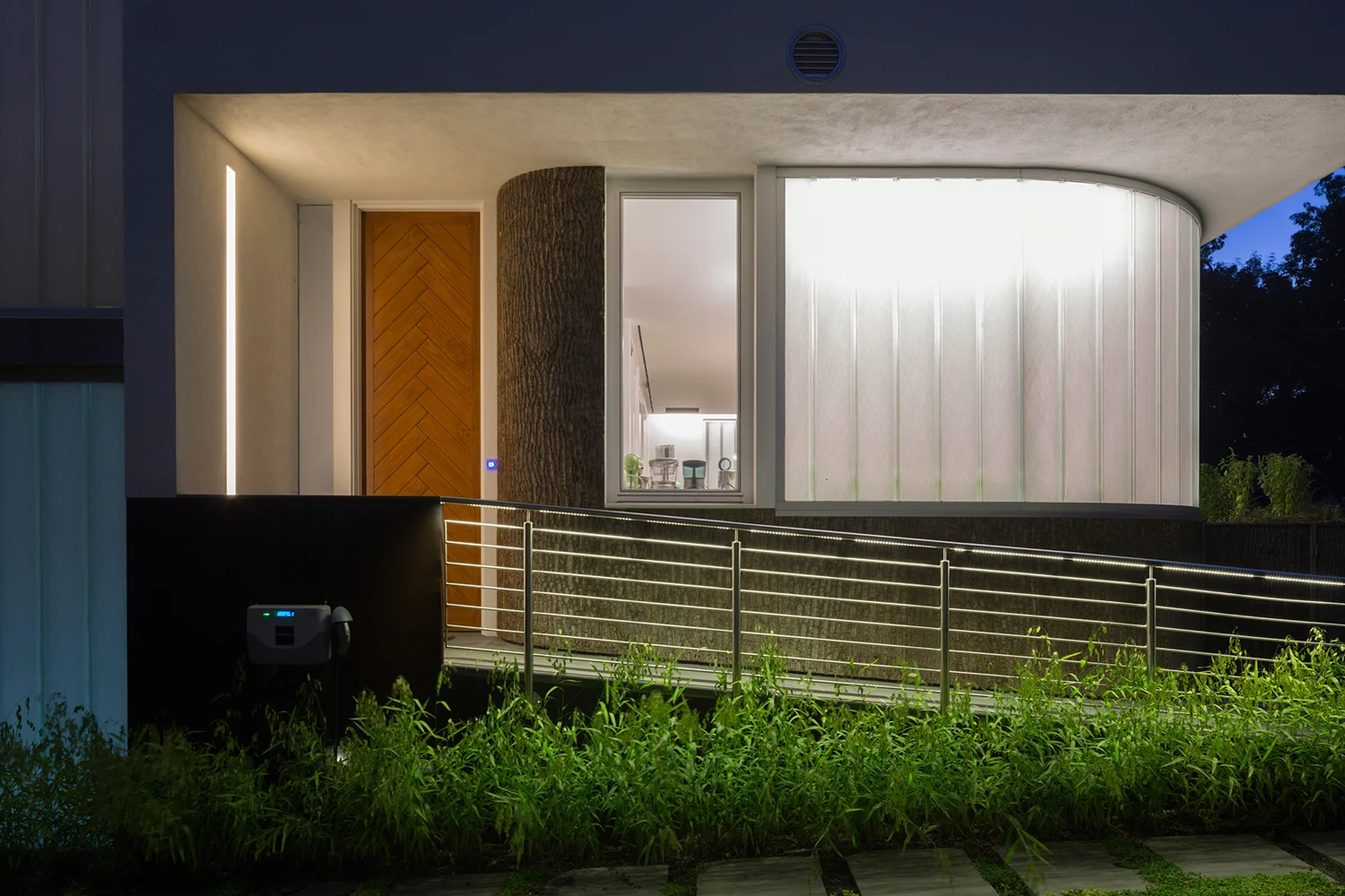 The entry ramp at night showing the glow of the curved channel glass front eh kitchen lights.