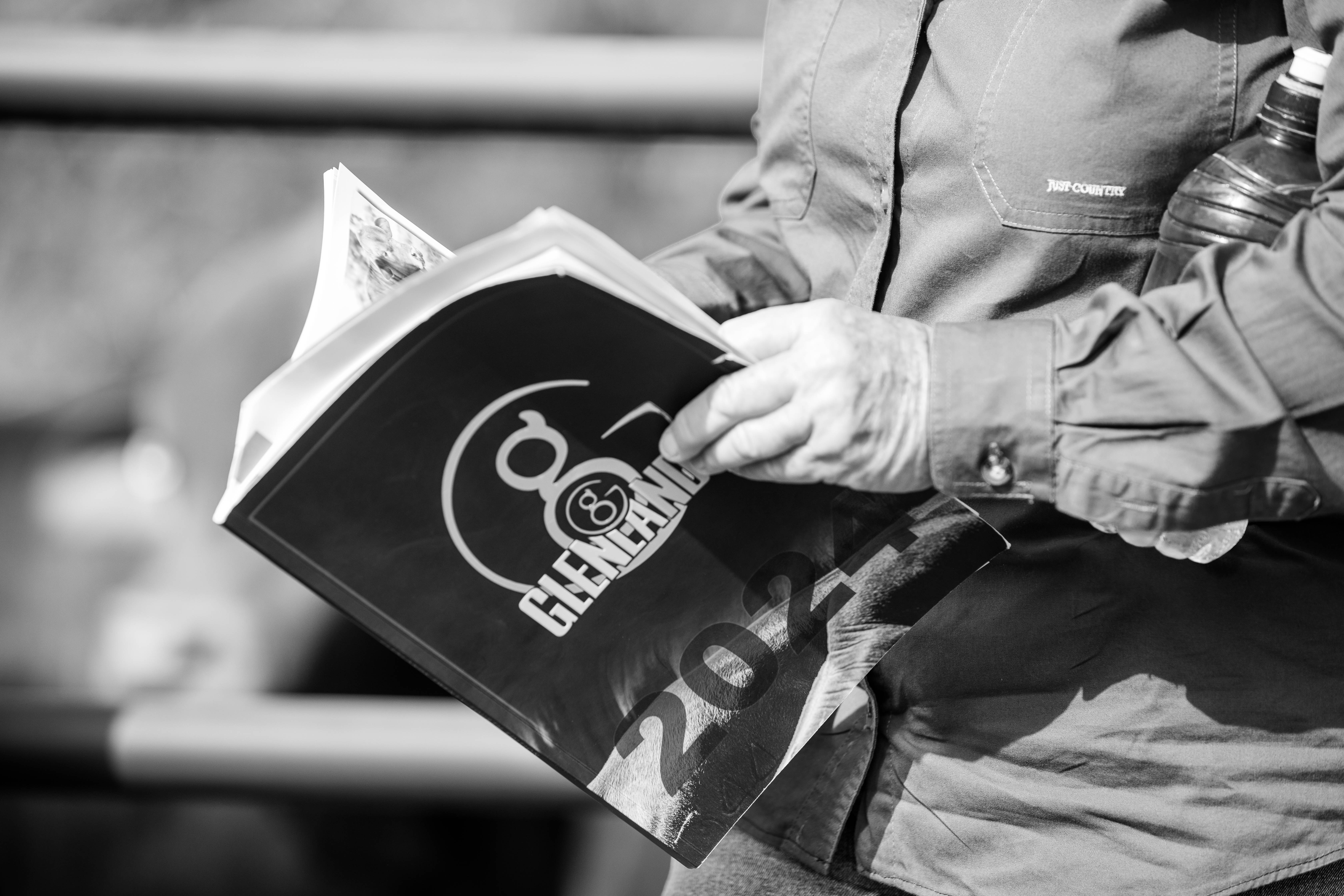 Person holding and reading a 2021 Gleneland catalog or program in black and white.