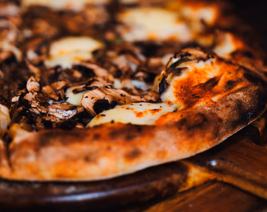 Close-up of a mushroom and cheese pizza slice with a golden-brown crust on a wooden board.