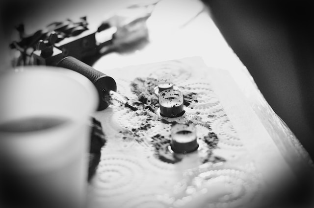 black and grey photo of tattoo ink and a tattoo machine with ink splatter 
