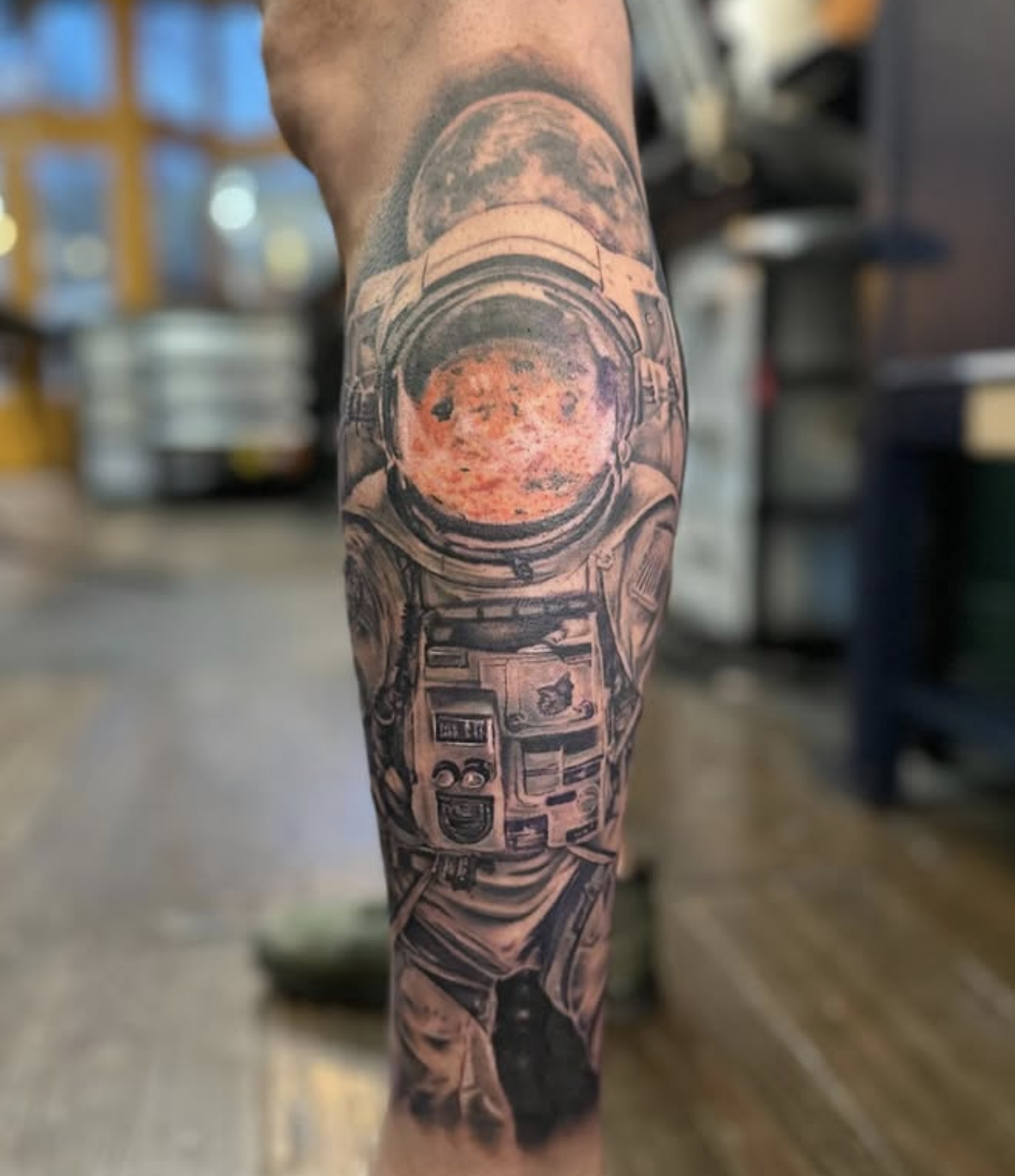 Tattoo of an astronaut with a colored reflection of a planet in the visor of the space suit by Noah Brewer