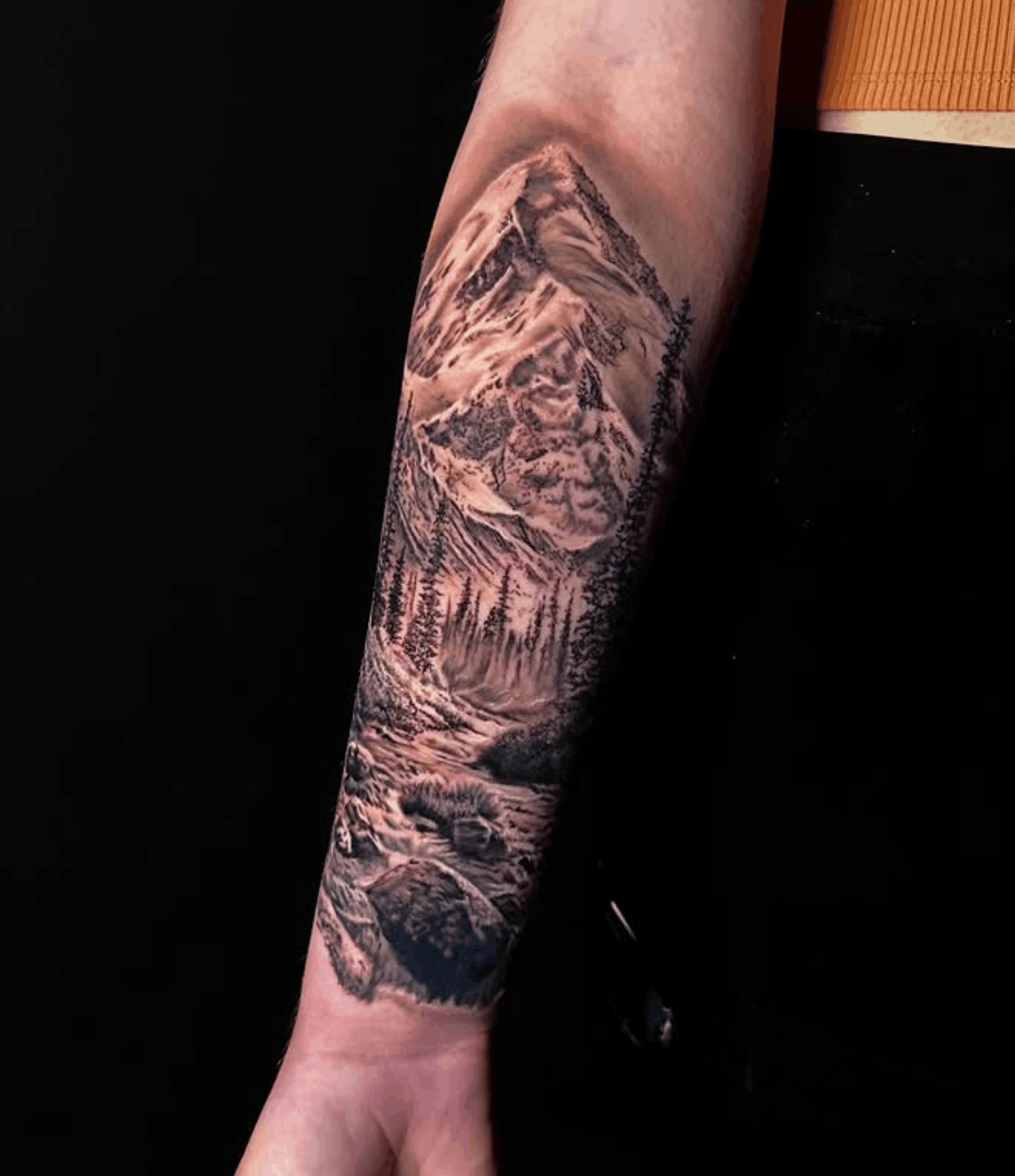 Tattoo of a mountain scene with trees and a river by Noah Brewer