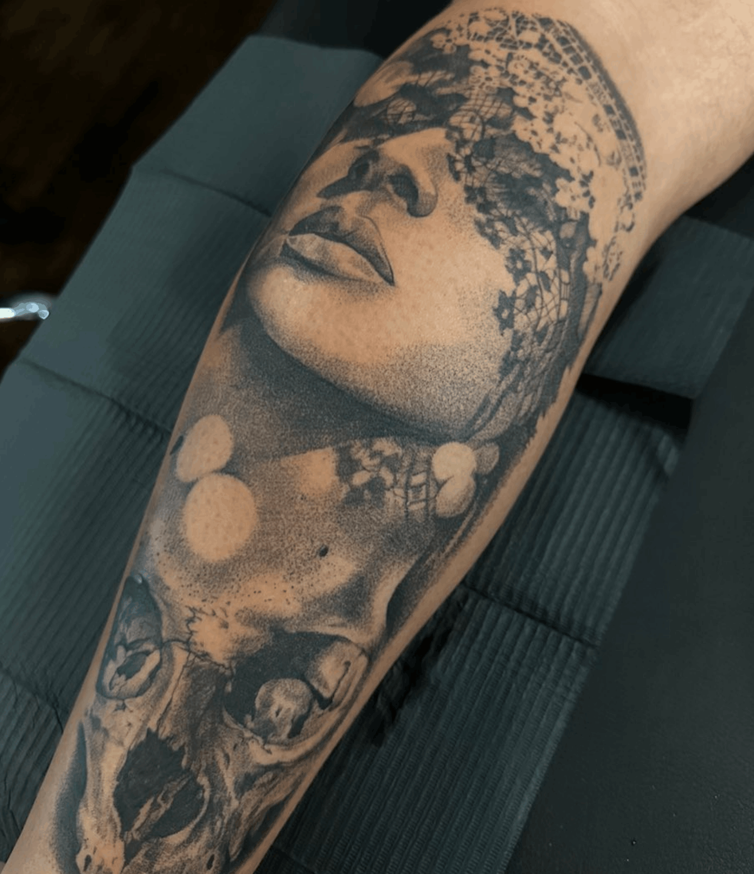 Tattoo of a womans face with lace and shadow over her eyes and a skull beneath the portrait by Noah Brewer