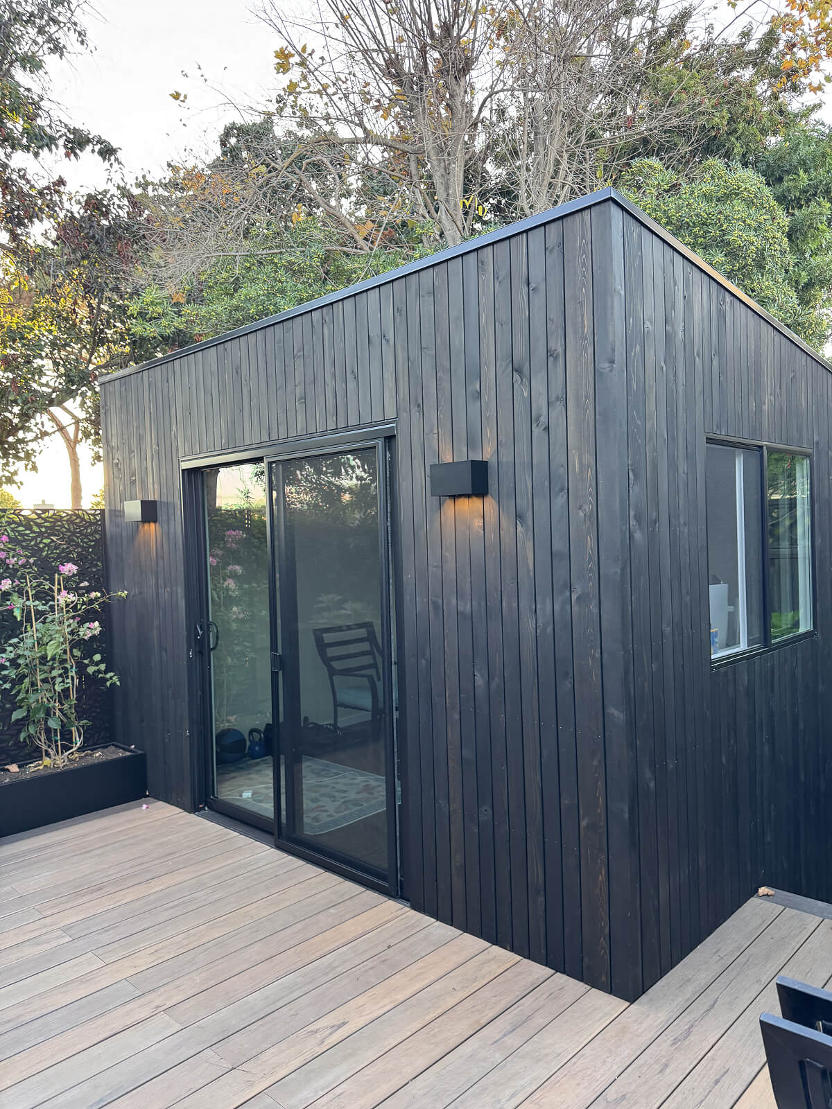 Minima backyard office shed with black vertical wood siding, large sliding glass door, insulated modern studio by Rivolty.
