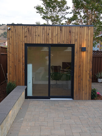 Minima backyard office shed by Rivolty with natural cedar exterior, insulated construction, and large sliding glass door.