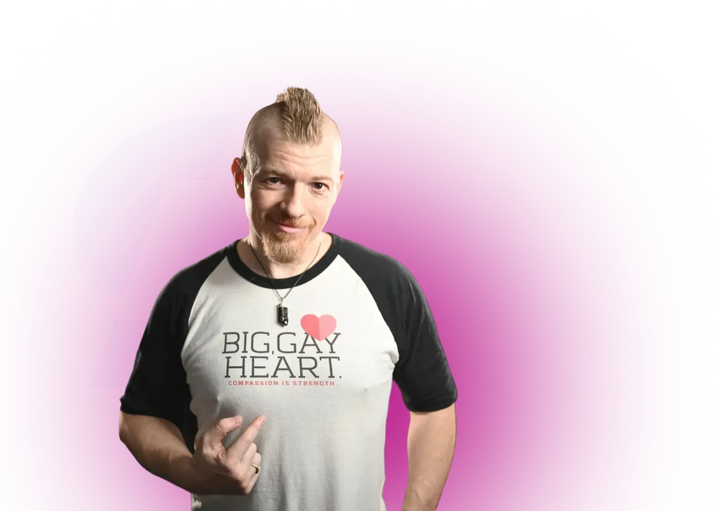 Man with a mohawk hairstyle wearing a white and black raglan shirt that reads 'BIG GAY HEART COMPASSION IS STRENGTH' on a magenta background.