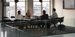Four professionals sitting around a table in a modern office meeting room with large windows.