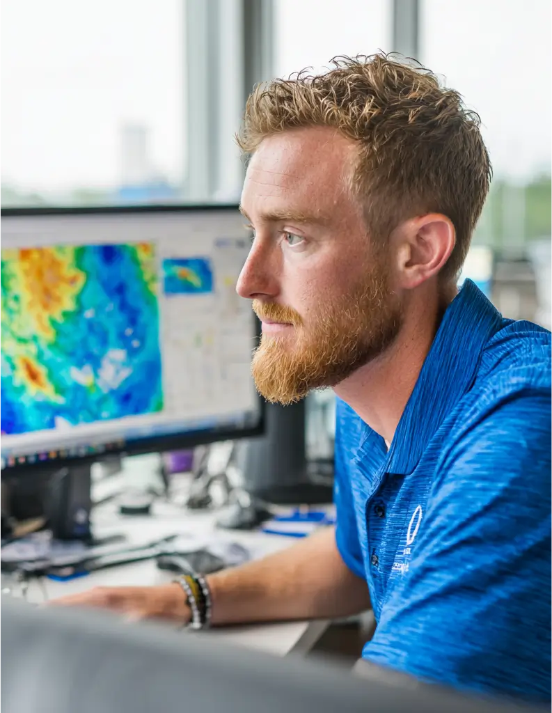 Man with curly hair and a beard closely studying colorful data on a computer monitor in an office.