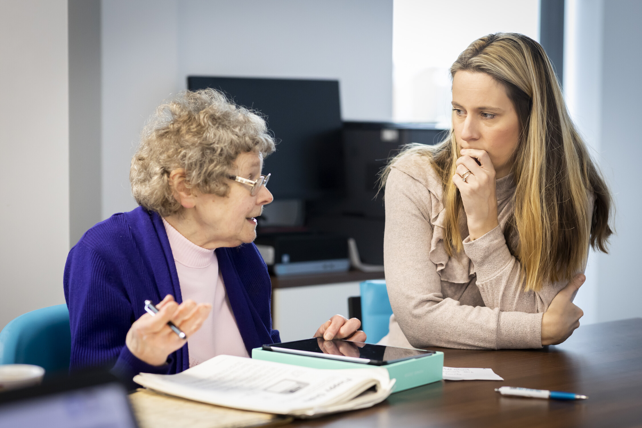 An older woman and a younger woman having a serious conversation with an ipad and paperwork on the table.