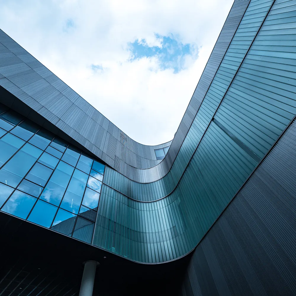 Curved modern building facade with reflective glass windows under a cloudy blue sky.