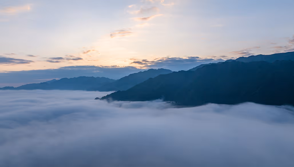 Mountain range at sunrise with a dense sea of fog covering the valley below.