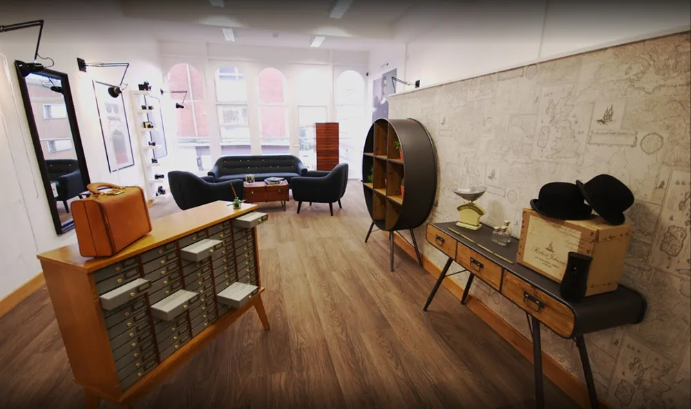 Modern lounge with wood floor, gray sofas, vintage suitcases, a round shelf, and a table with hats and decor.