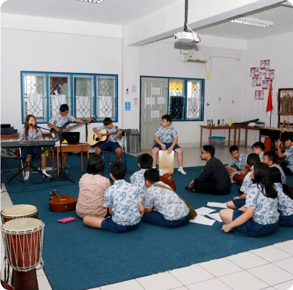 Sekolah Bogor Raya's Primary School Music Room. Students in matching uniforms in a music room playing instruments and listening on a blue carpet.