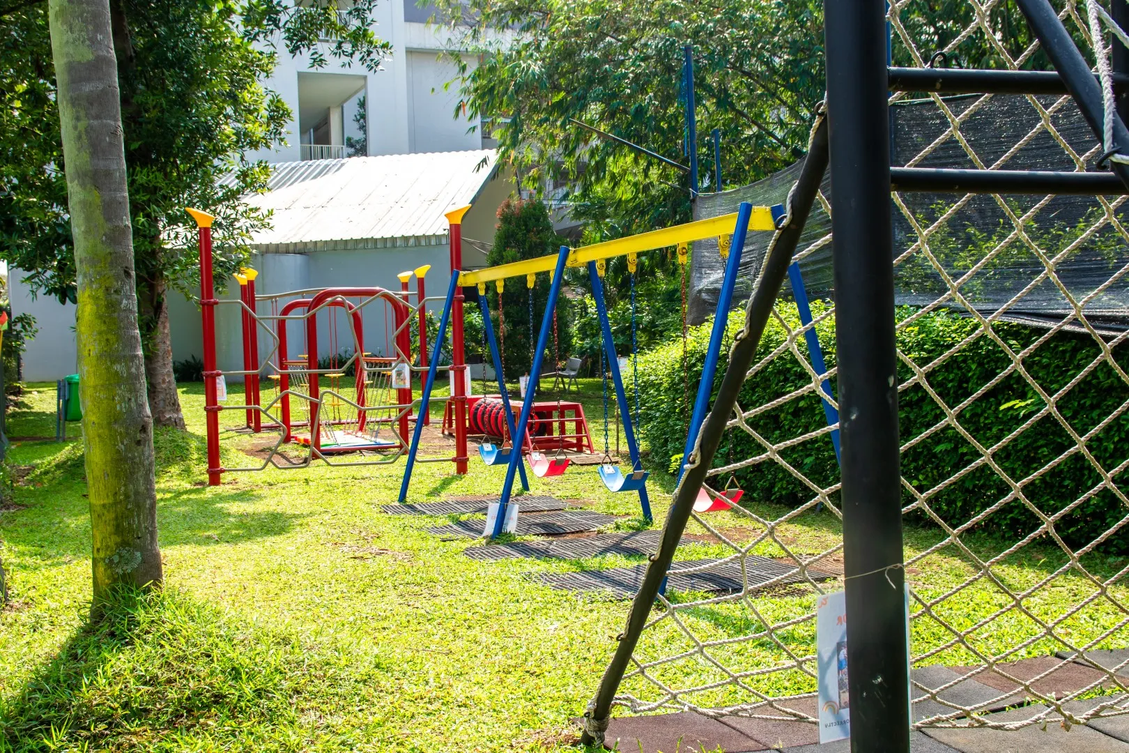Sekolah Bogor Raya's Primary School outdoor playground with swings, climbing nets, and red and yellow play structures on grass.