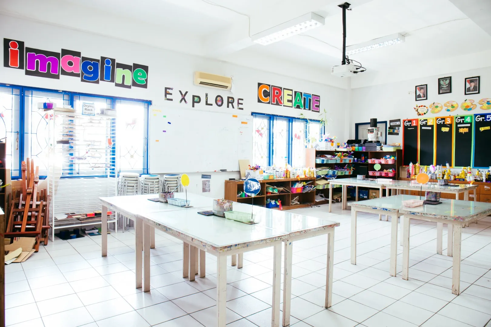 Sekolah Bogor Raya's Primary School Art Room. Bright art classroom with white tables, colorful words imagine explore create on walls, and art supplies neatly stored.