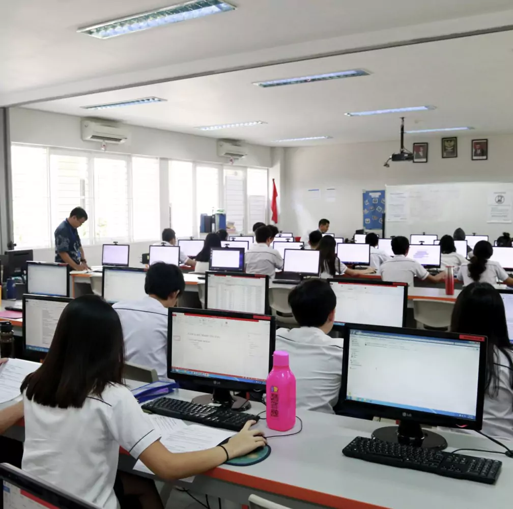 Sekolah Bogor Raya's Secondary School ICT Lab. Students in white uniforms working on desktop computers in a bright, modern computer lab classroom.