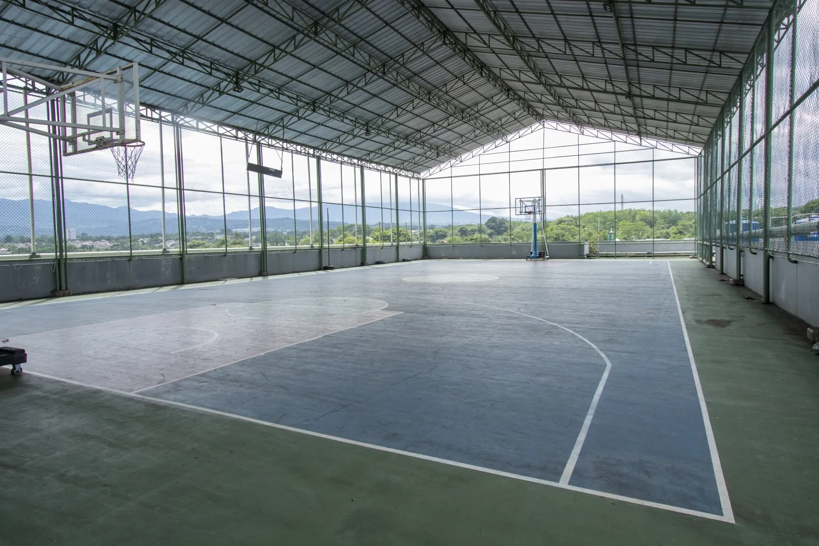 Sekolah Bogor Raya's Secondary School Basketball Court. Covered outdoor basketball court with two hoops and a chain-link fence around it.