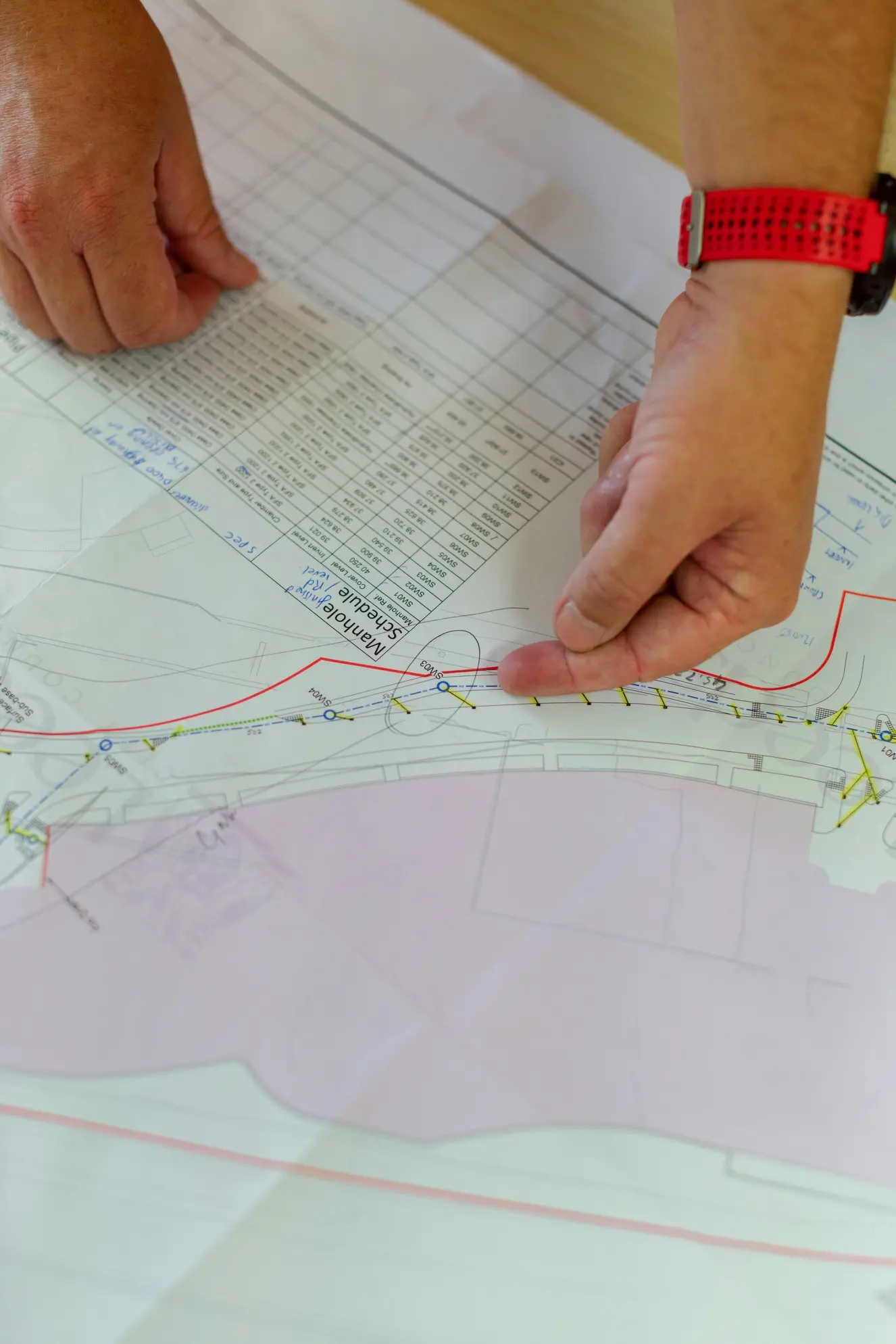 Two hands pointing to a marked location on a detailed technical map or plan with a schedule table.