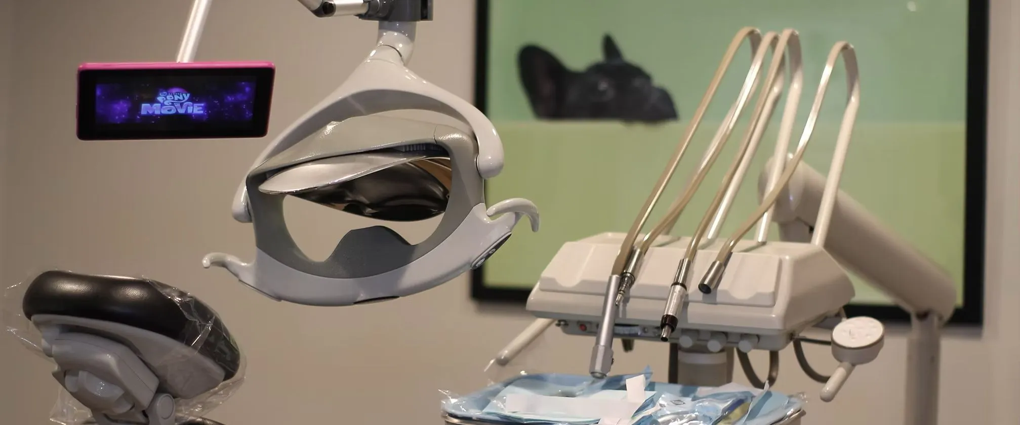 Close-up of a dental chair with overhead dental light, dental instruments, and a small screen displaying 'My Little Pony Movie'.