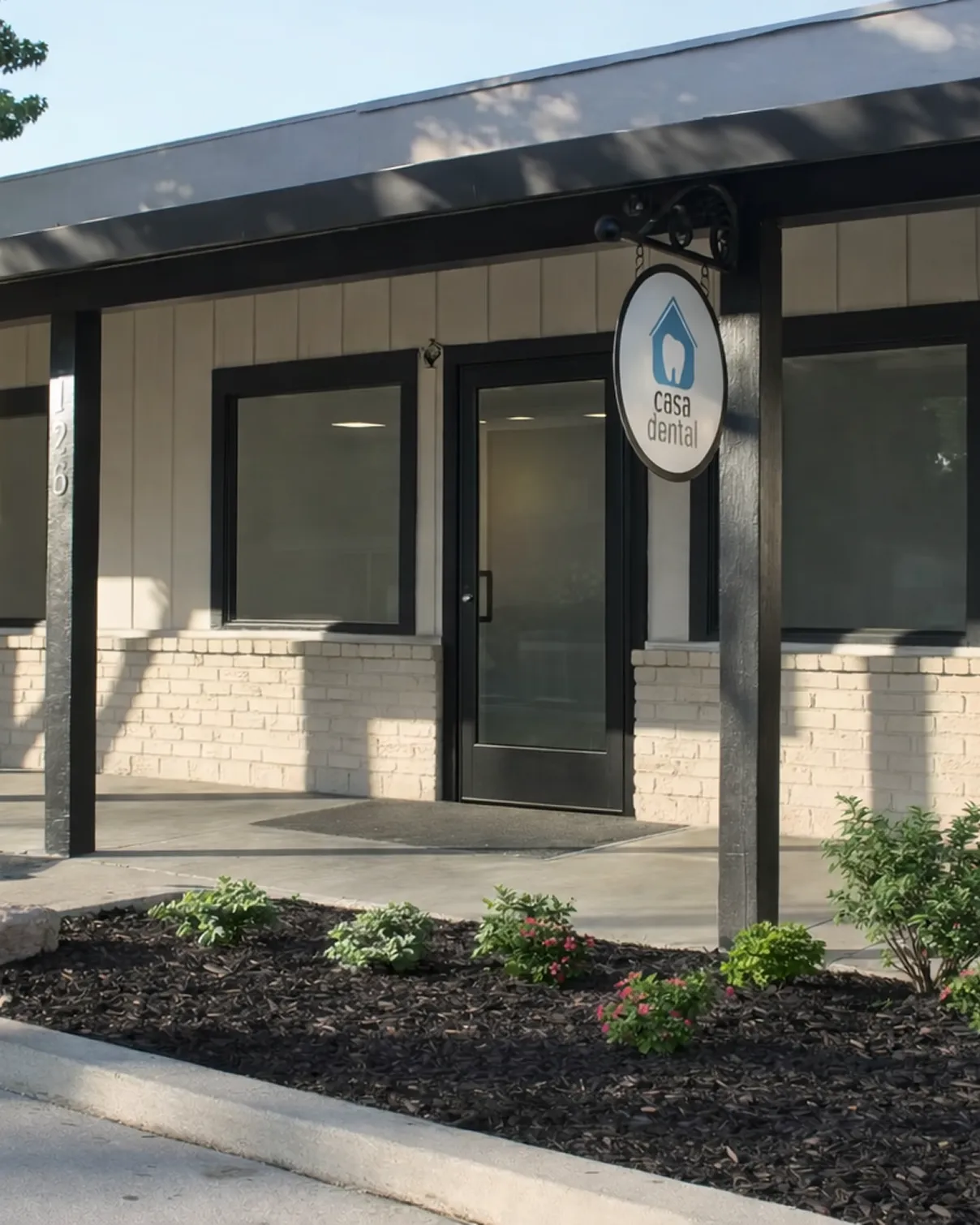 Entrance of a dental clinic with a black door, two windows, and a hanging sign displaying a tooth inside a house icon and the text 'casa dental'.