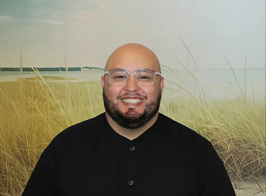 Smiling bald man with a beard wearing clear glasses and a black shirt with a white tooth logo on the chest.