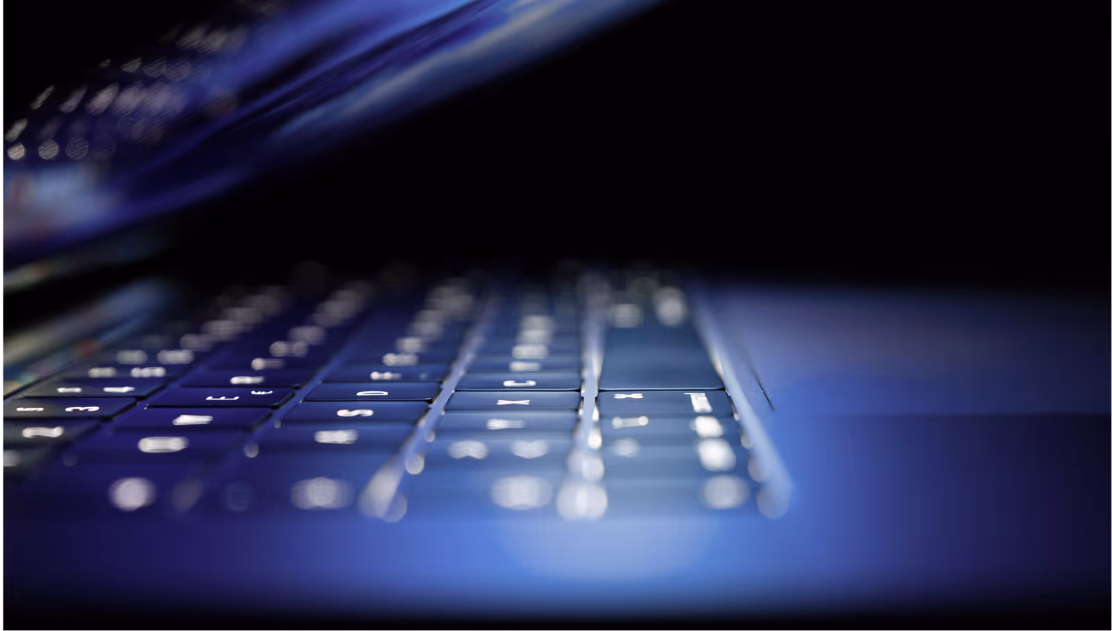 Close-up side view of a laptop keyboard with blue lighting and blurred background.