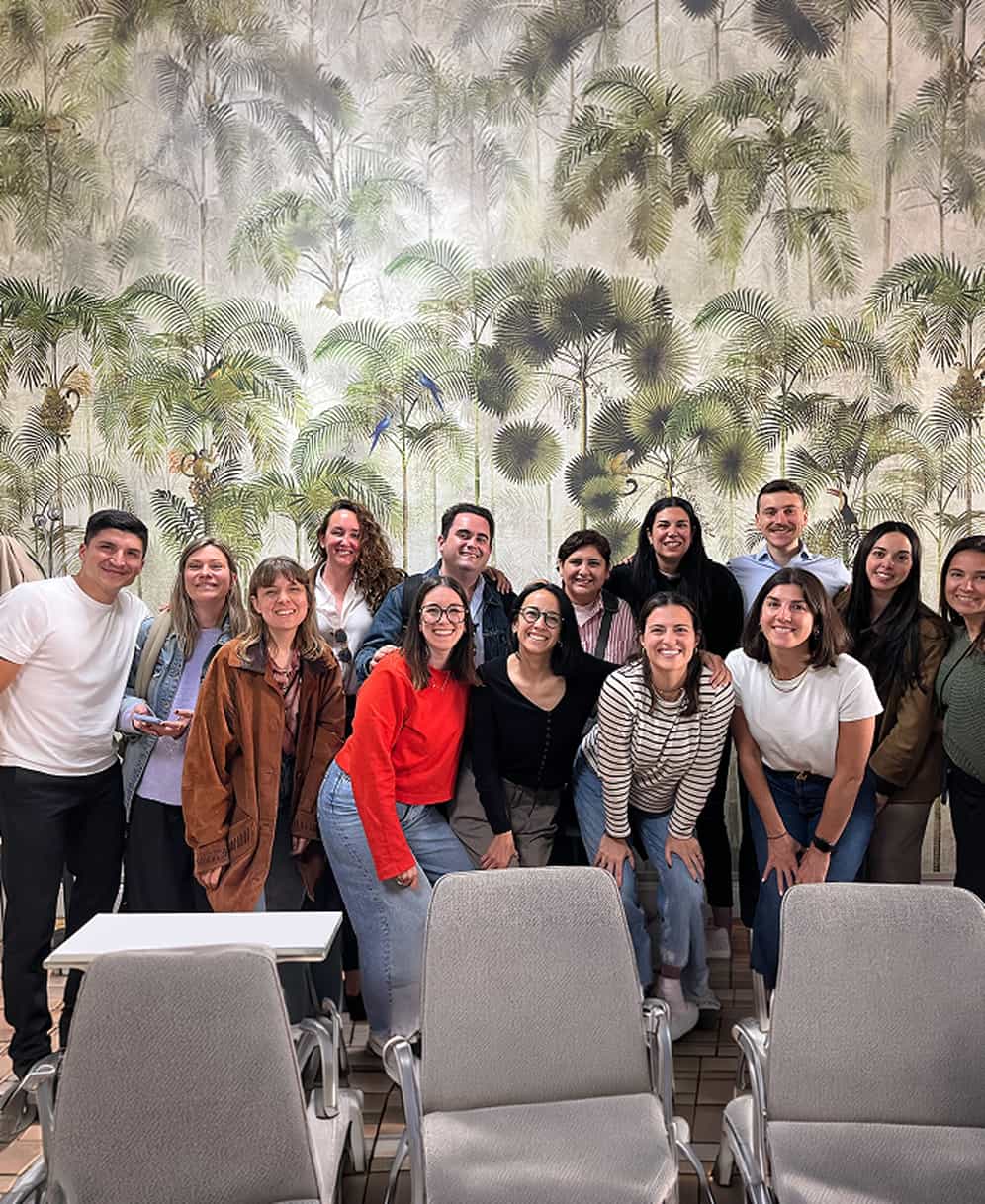 Grupo de personas sonriendo frente a un mural con plantas y aves tropicales.