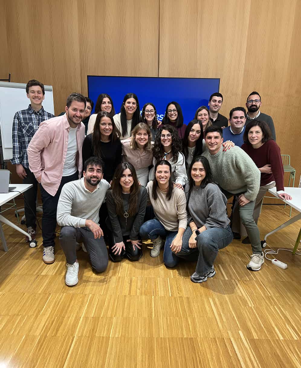 Grupo de personas posando y sonriendo en una sala con paredes de madera y pantalla azul.