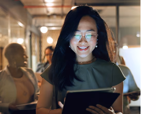 Smiling professional using a tablet in a modern office with colleagues in the background.