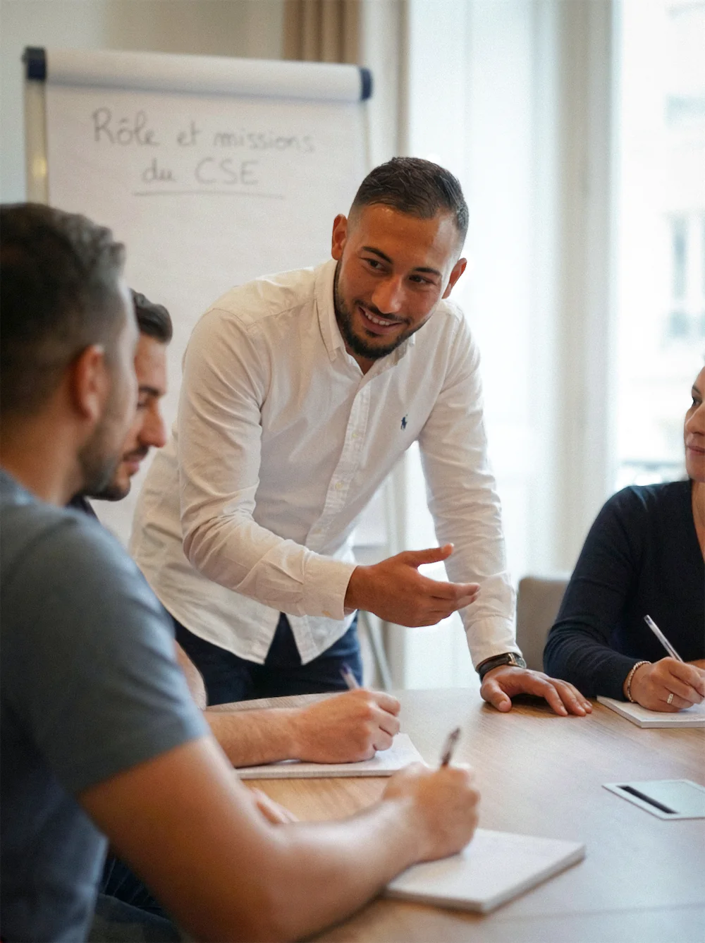 Formateur CSE en chemise blanche expliquant le rôle et les missions du CSE à un groupe d'élus assises autour d'une table.