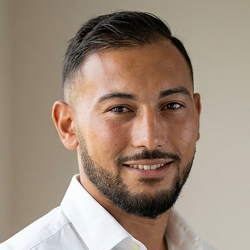 Portrait de Mehdi El Haimeur, gérant et formateur CSE, portant une chemise blanche, avec une barbe soignée et les cheveux coiffés en arrière, sur fond neutre.
