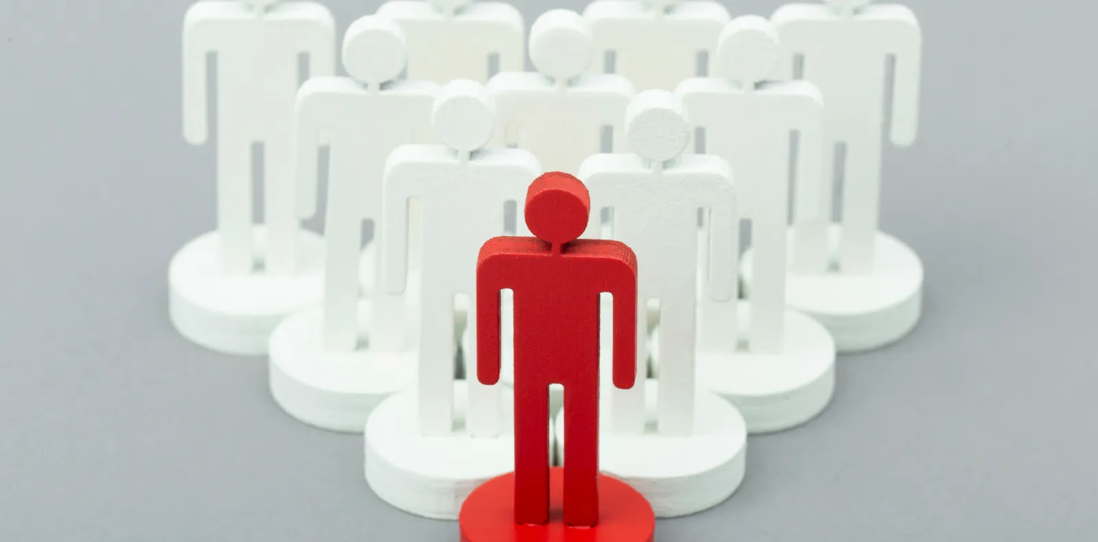 Worth Recruiting Toronto. Red wooden figurine standing in front of a group of white wooden figurines arranged in a pyramid shape on a gray background.