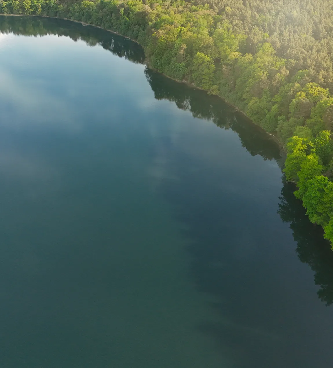 Aerial drone view of a calm, dark blue river winding through a lush, dense green forest.