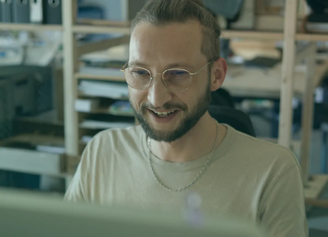 Portrait of a smiling team member with glasses and a beard working at a computer in the office.