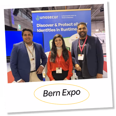 Three people smiling and standing in front of a trade show booth with a banner that says 'unosecur Discover & Protect all your Identities in Runtime'.