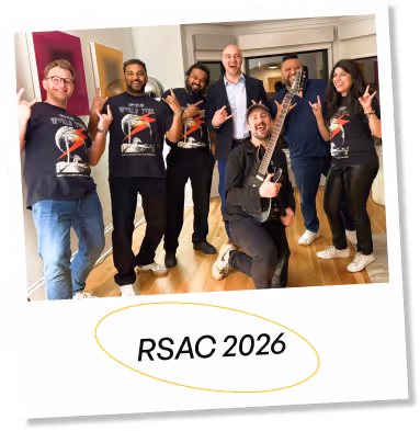 Group of six people, five standing and one kneeling with an electric guitar, all making rock hand signs and smiling, with text 'RSAC 2026' below them.