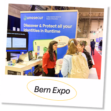 Three people talking in front of a unosecur booth displaying 'Discover & Protect all your Identities in Runtime' at Bern Expo.