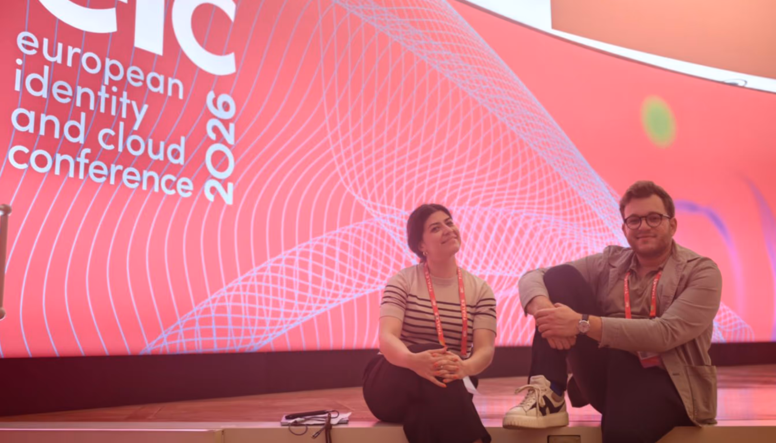 Panel discussion with four speakers seated, one woman speaking into a microphone while a man stands at a glass table nearby.