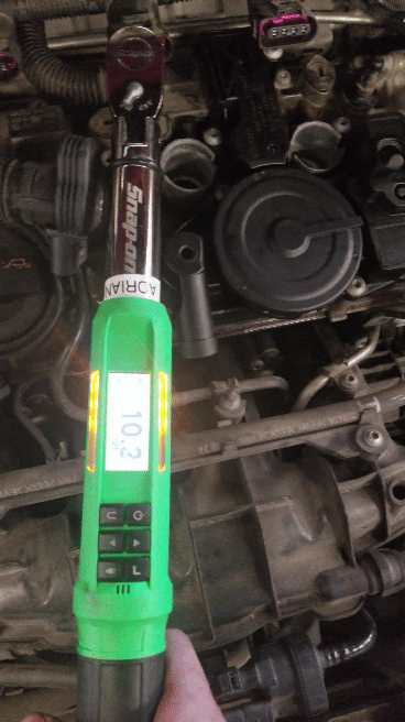 Digital torque wrench displaying 10.3 while tightening a bolt on a car engine.