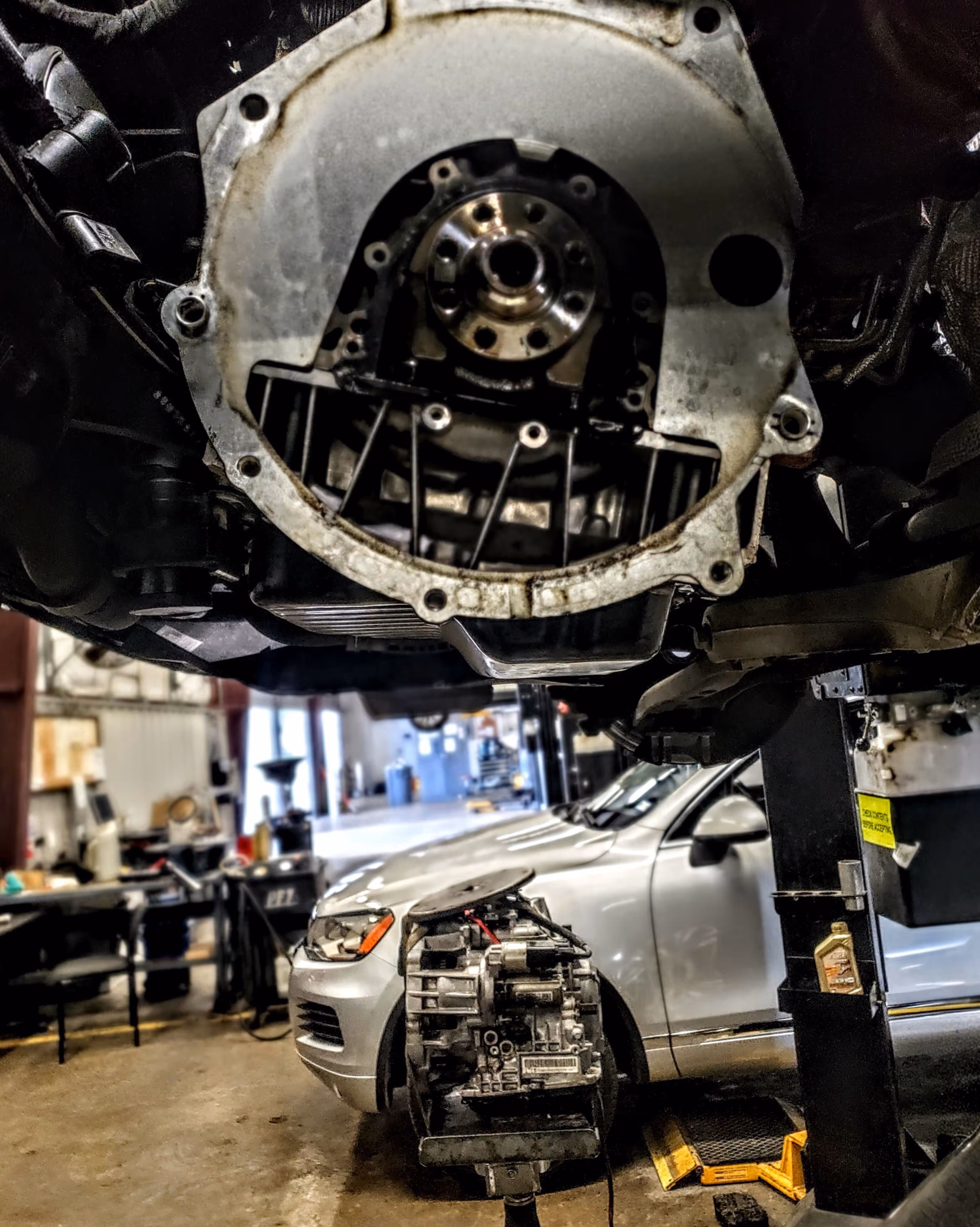 Close-up of a mechanical part in a car repair shop with a silver car and other tools in the background.