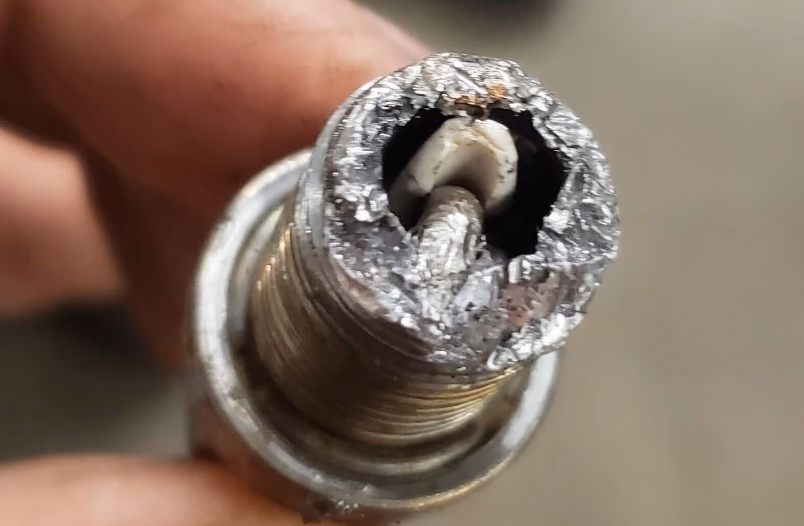 Close-up of a severely damaged and corroded spark plug with eroded electrode and deposits around the tip.