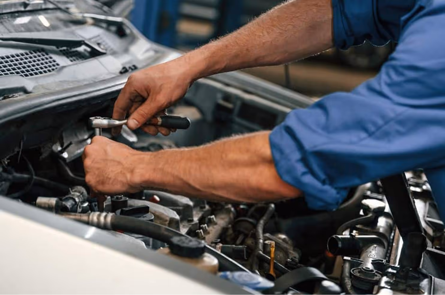 Mechanic using a ratchet wrench to work on a car engine under the open hood.